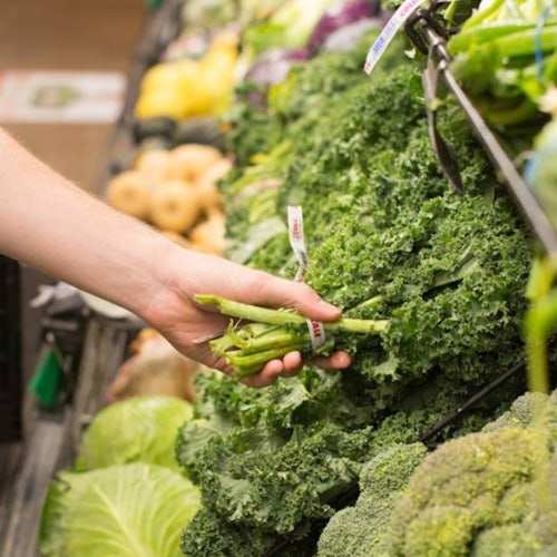 Produce section of grocery store womans hand reaching out to pick brocolli