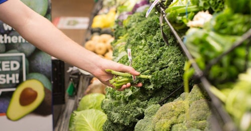 Produce section of grocery store womans hand reaching out to pick brocolli